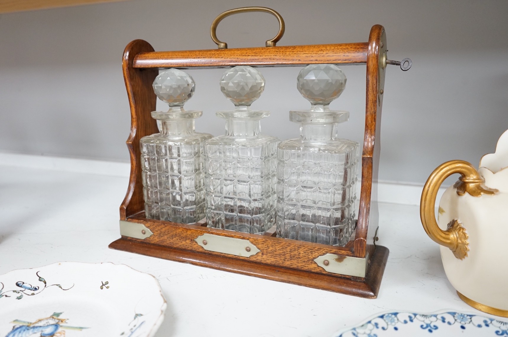 An oak three bottle tantalus, with key, together with three 18th/19th century faience plates and a Royal Worcester jug, tantalus 36cm wide